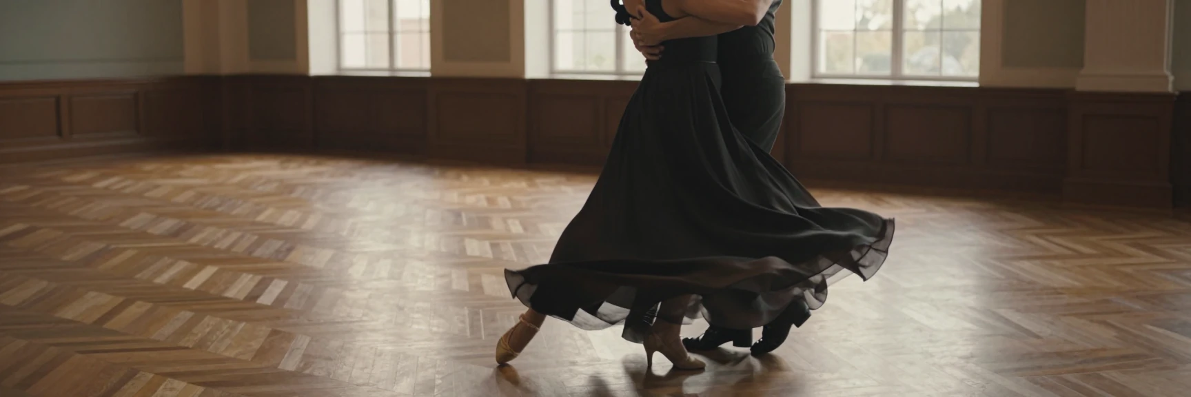 Un couple tourne une valse sur le parquet d’une grande salle, la robe longue déployée par le mouvement