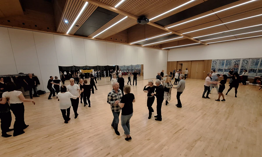 Une piste pleine de couples de danse de salon lors d’une soirée pratique, dans une grande salle aux murs de miroirs